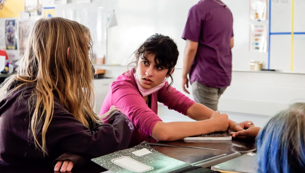 a girl in a pink shirt listens to another student