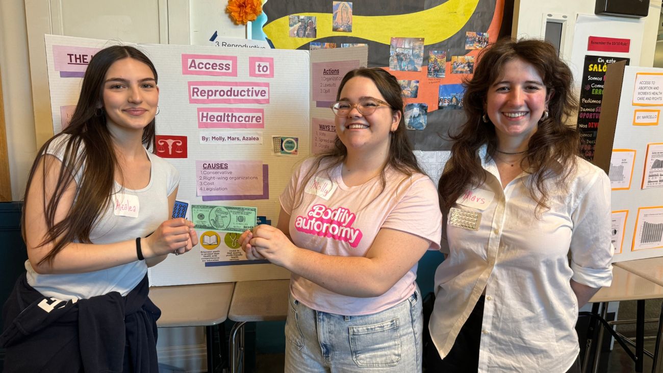 Two female students and a female teacher smiling and presenting a picture